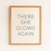 Framed wall art print with the text 'There She Glows Again' in a simple, modern font on a light background.